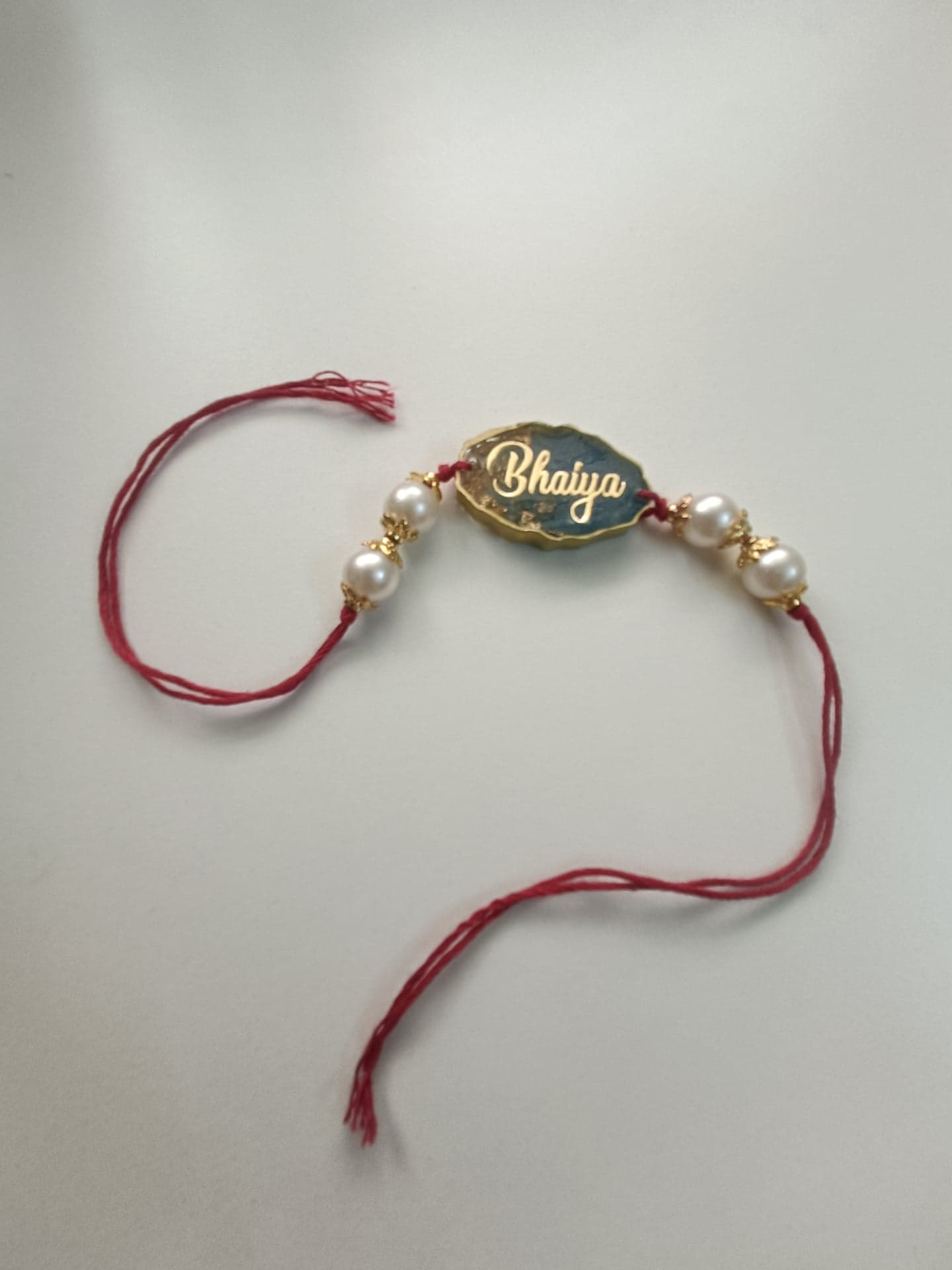 Resin rakhi with gold Bhaiya lettering, pearls and red thread