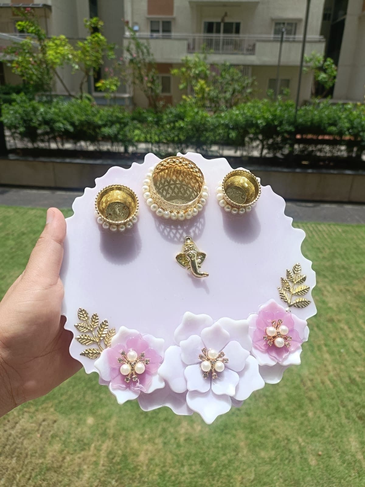 Lavender resin pooja thali with pink and white flowers, diya cups and a Ganesha charm